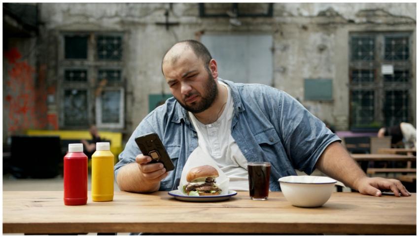 Bald bearded man sitting outdoors holding smartpho