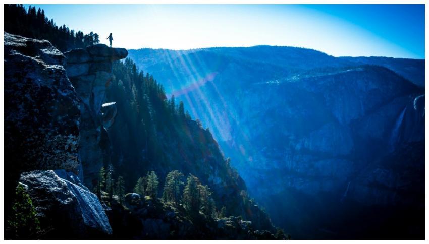 Silhouette of a person on a cliff with mountains a