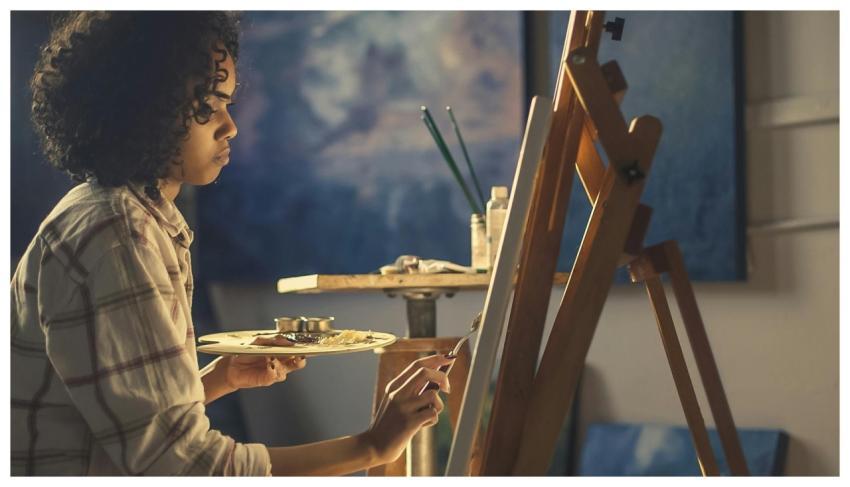 Side view of a young woman artist painting on canv