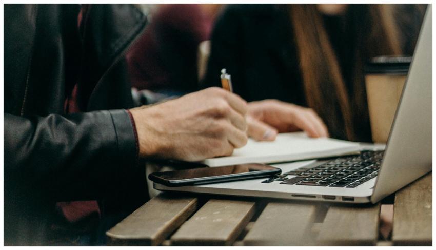 A freelancer writing notes in a notepad beside a l