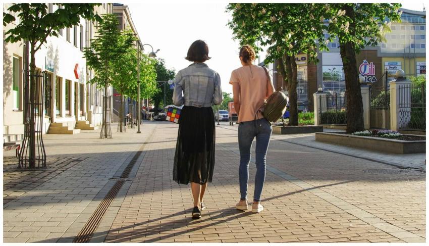 Two women enjoy a sunny walk down a lively urban s