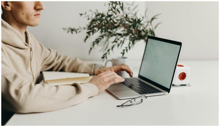 A young man in a hoodie works on a laptop next to