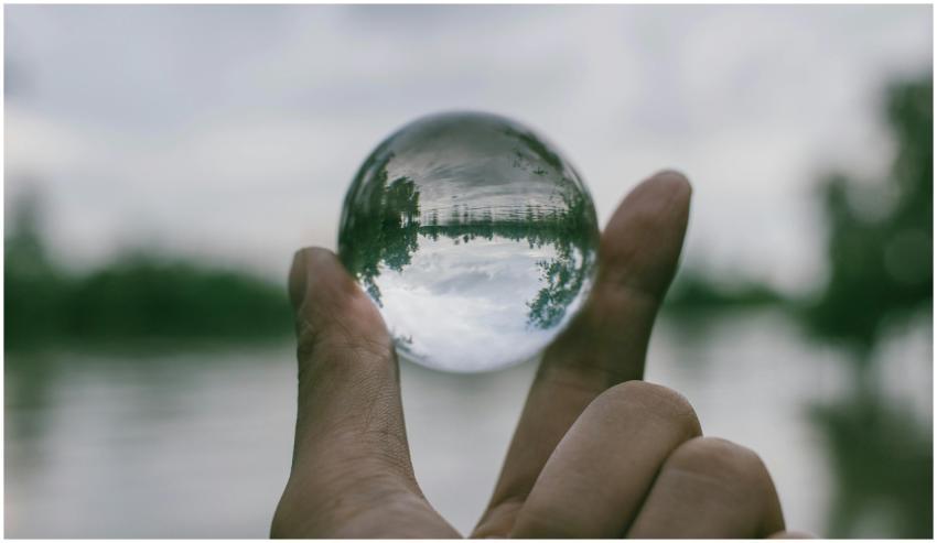 A hand holding a transparent glass sphere outdoors