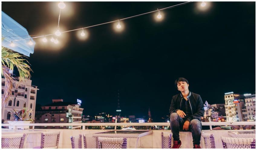 Asian man sitting on rooftop at night with city li