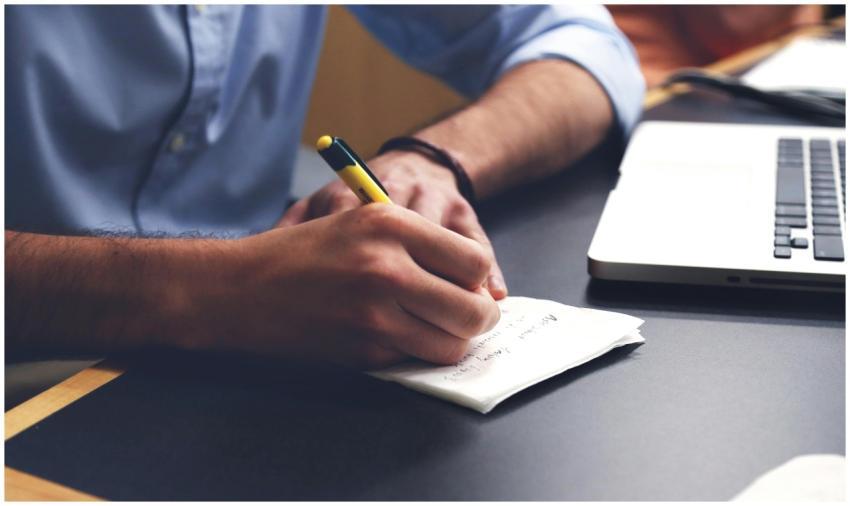 Close-up of a man writing notes with a pen next to