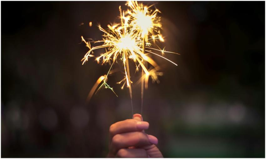 A hand holding sparklers glowing brightly in a dar
