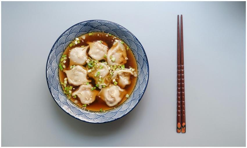 Top view of a bowl of dumplings in soup garnished