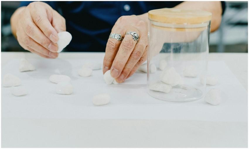 Hands arranging white pebbles on a table in a mini