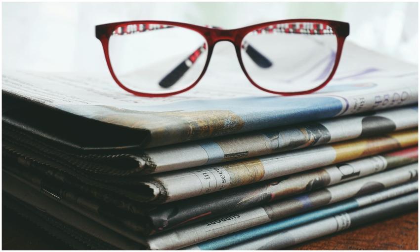 Red eyeglasses resting on a stack of newspapers sy
