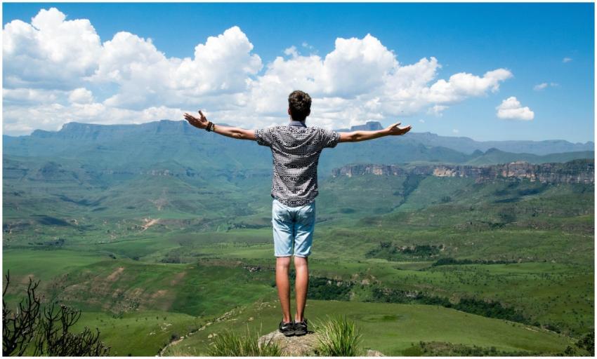 A man stands triumphantly with arms open, overlook