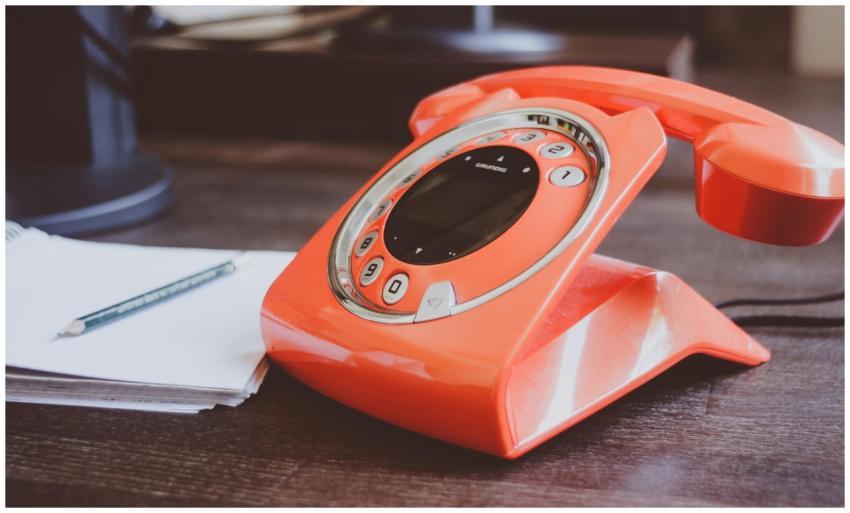 A retro-style orange rotary phone sits on a wooden