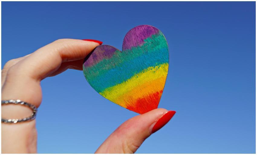A hand holding a rainbow-colored heart against a c