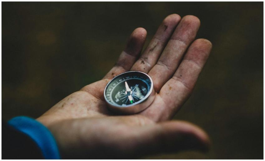 A close-up of a compass held in a dirty hand, symb