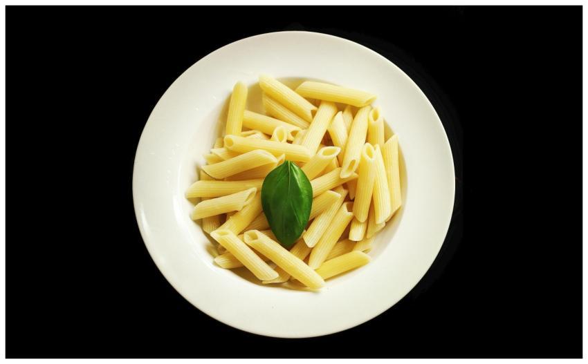 A simple white plate of penne pasta garnished with