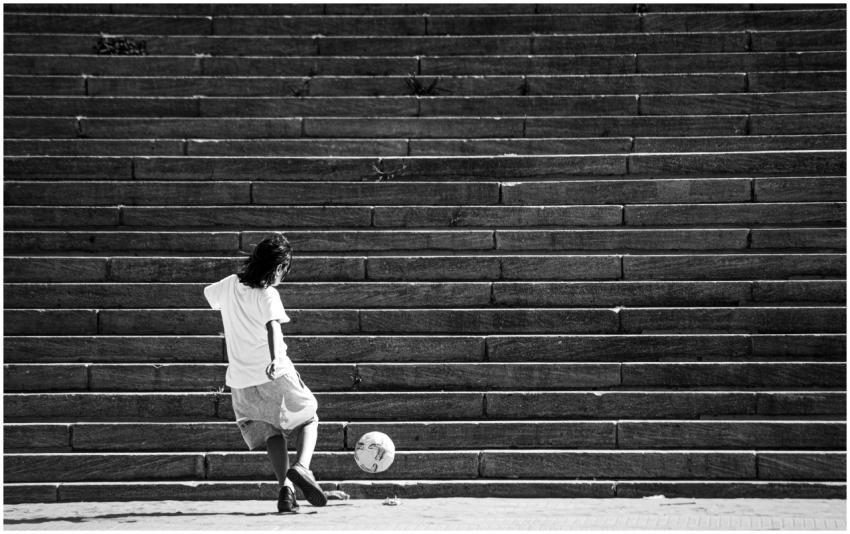 Black and white photo of a child kicking a soccer