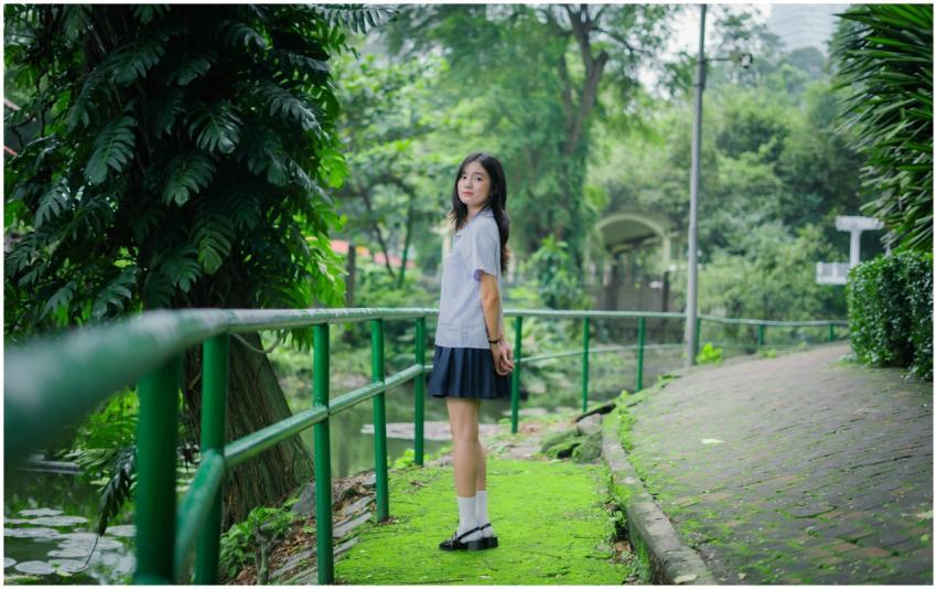 A young woman in a school uniform stands on a gree