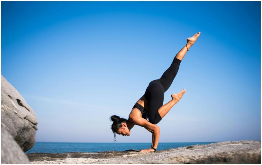 Woman performing a yoga pose on a rocky beach with