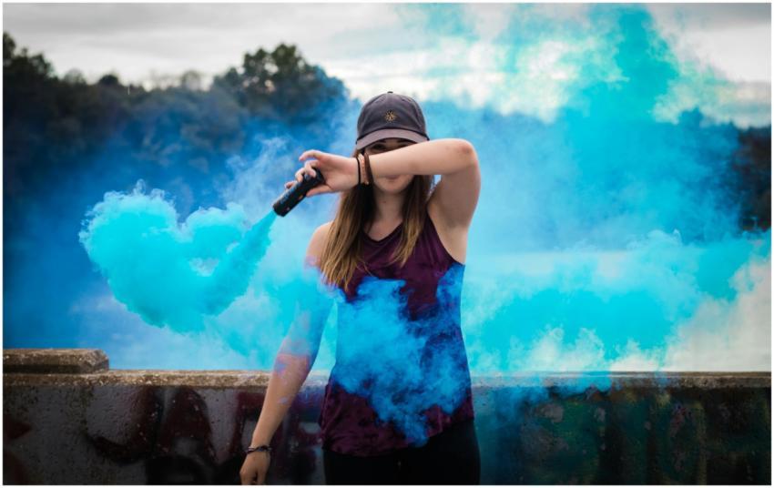 A stylish woman surrounded by bright blue smoke ou