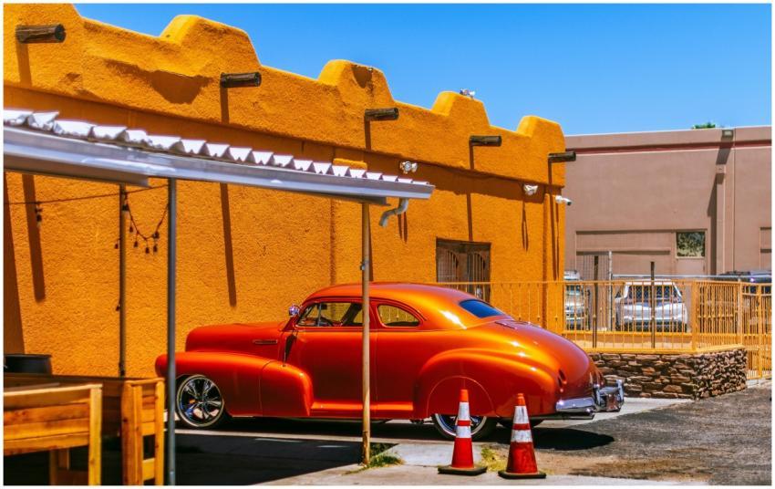 Vintage orange Chevrolet coupe parked by a vibrant