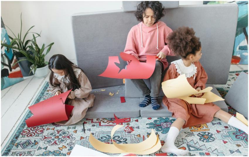 Three children sitting indoors, cutting colorful p