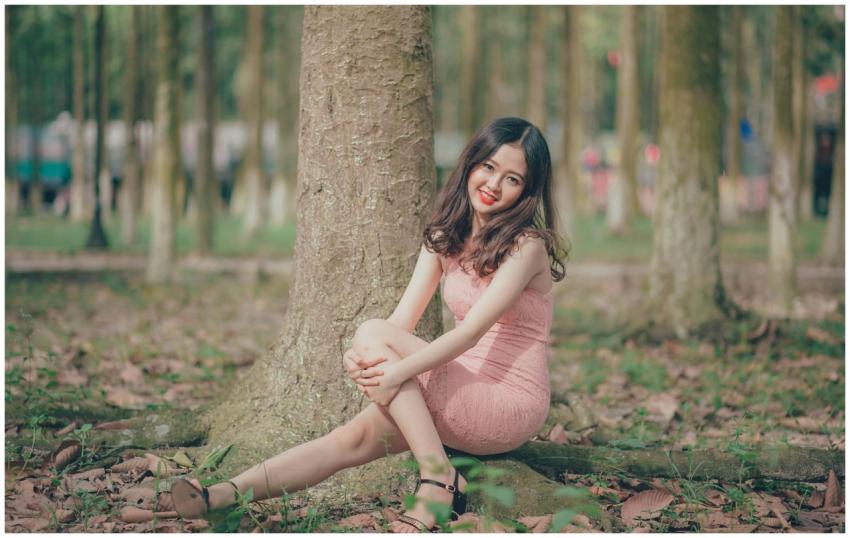 Smiling young woman sits against a tree in a sunny