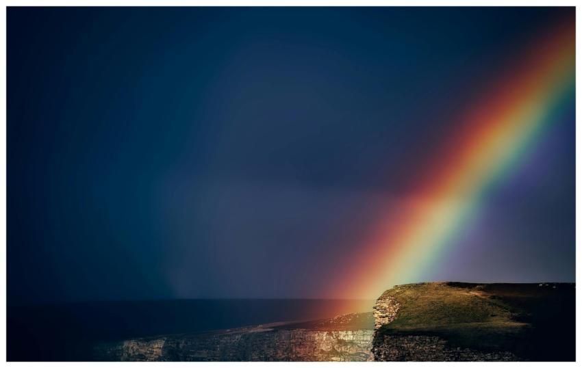 A vibrant rainbow arches over dramatic coastal cli