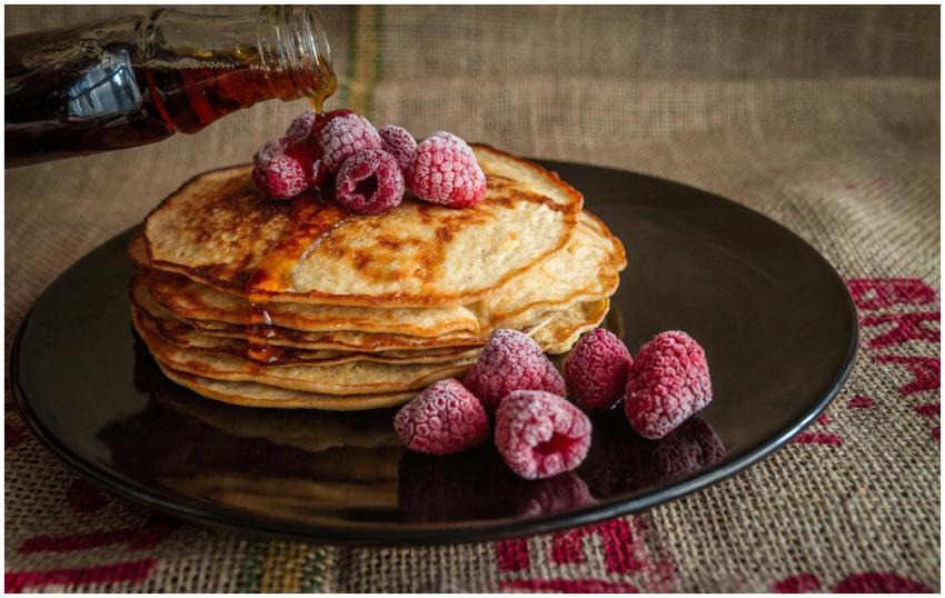 Stack of pancakes topped with raspberries and syru