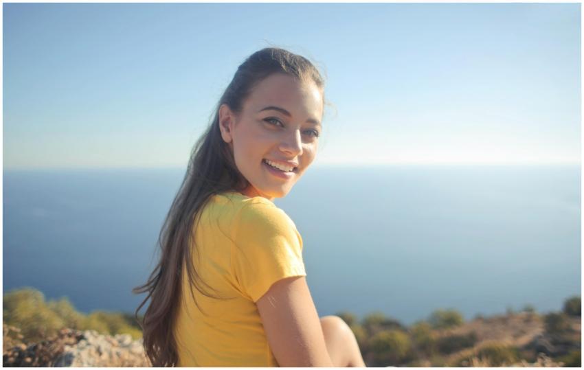 Young woman in a yellow shirt smiles by the sea, e