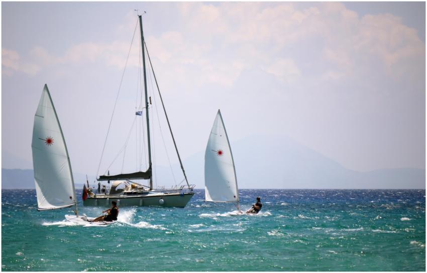 Two sailboats and a windsurfer on a sunny ocean da