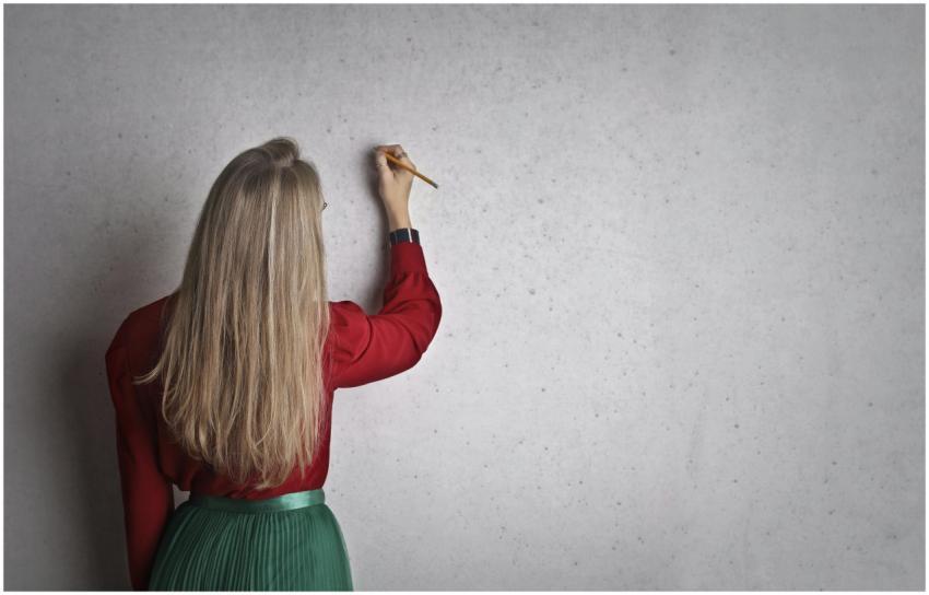 A woman in a red blouse writing on a concrete wall