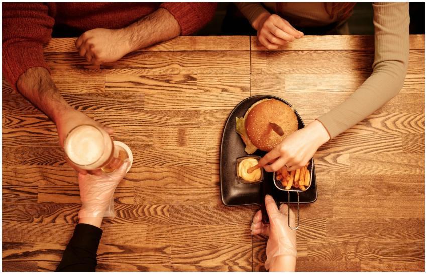 Top view of hands sharing a burger, fries, and bee