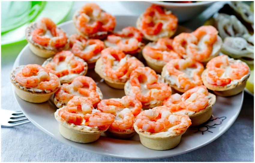 Peeled red boiled shrimps on tartlets on white pla