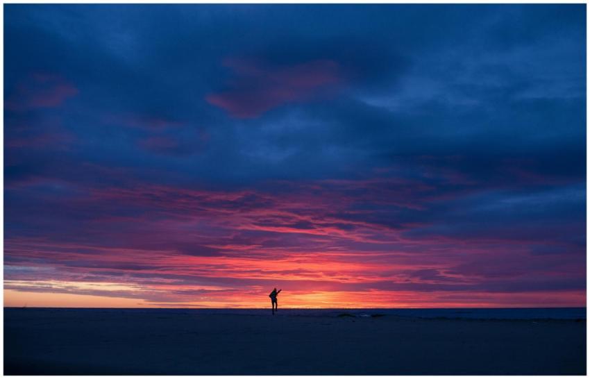 A lone silhouette stands against a vibrant sunset