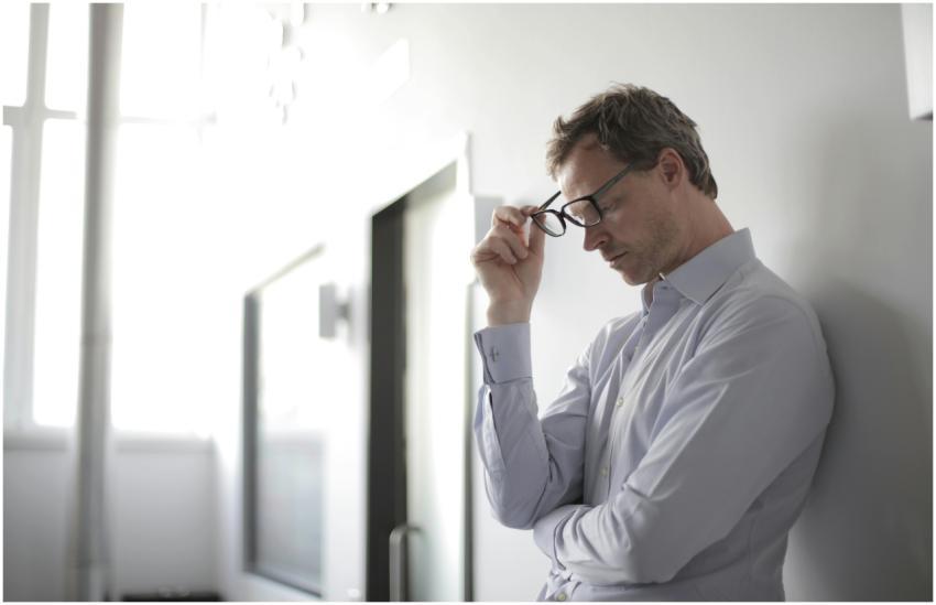 Thoughtful man in a bright room holding his glasse