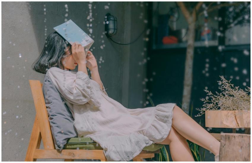 A young woman covers her face with a book while si