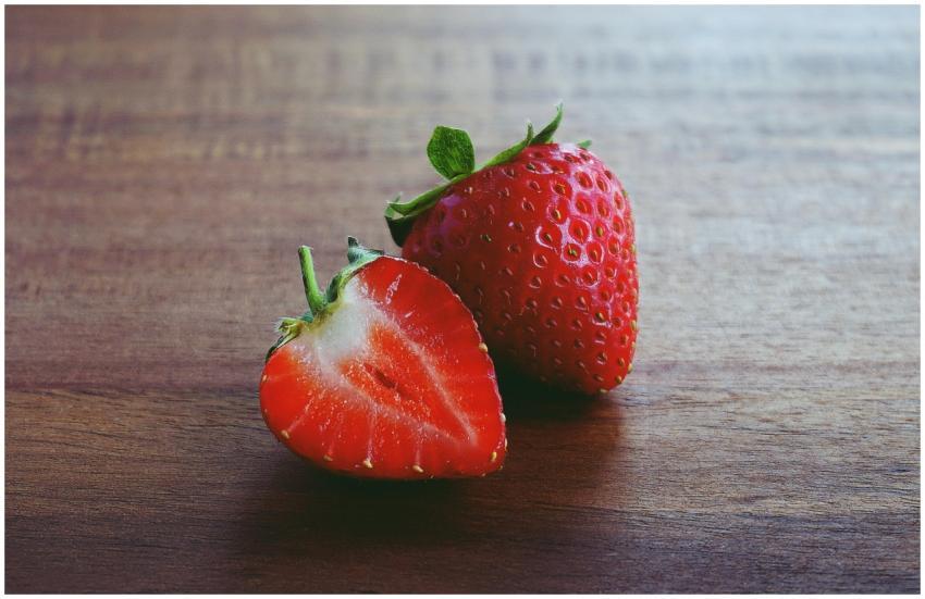 Two fresh strawberries, one whole and one sliced,