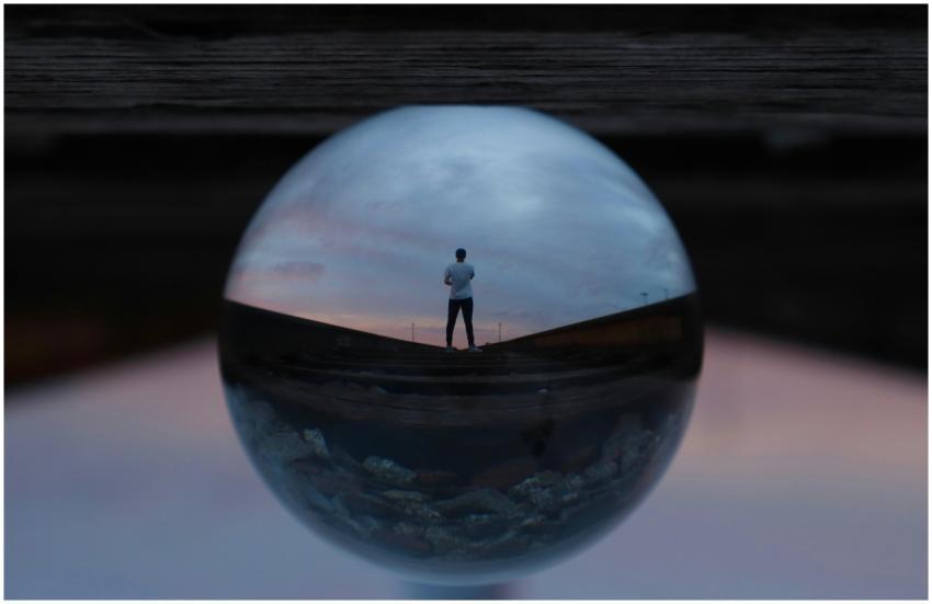 A man stands on train tracks, reflected in a glass