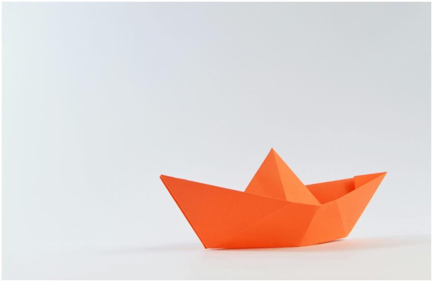 Minimalist image of an orange origami paper boat o