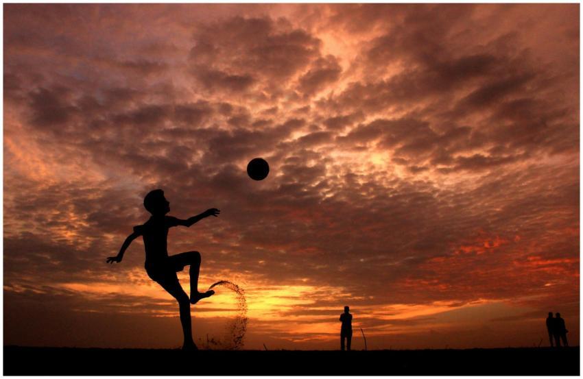 A child playing soccer on the beach at sunset in K