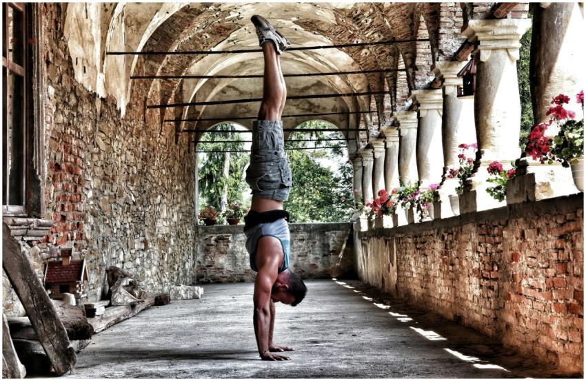A man performs a handstand in a rustic, arched cor