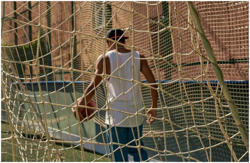 Person holding a basketball behind a net on a city