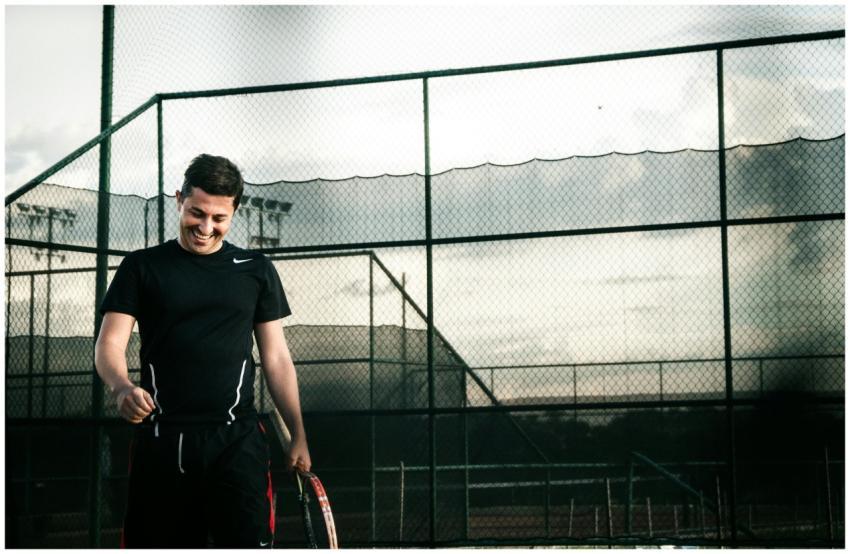 A happy tennis player smiles while holding a racke