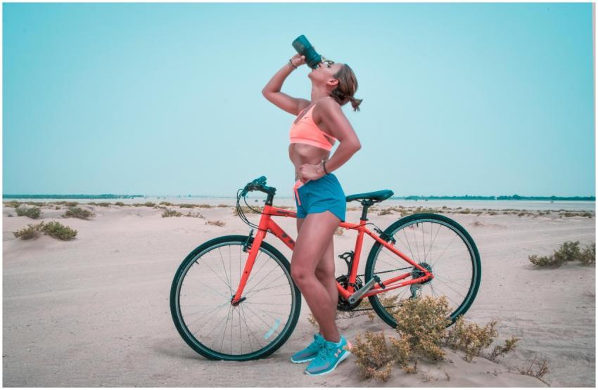Athletic woman drinking water while biking in the