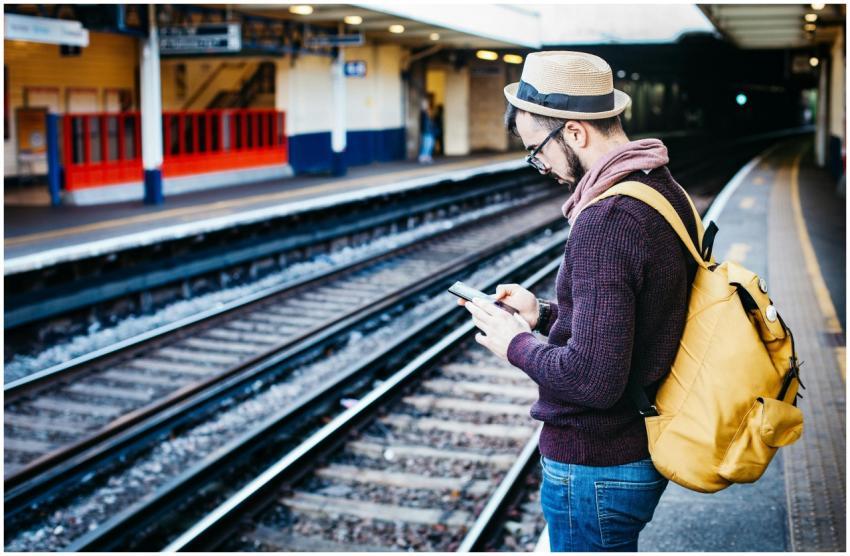 Man with backpack uses phone at urban train statio