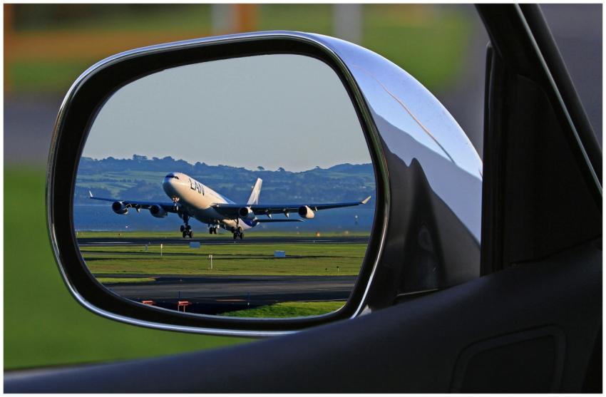 A jet airplane taking off is reflected in a car's