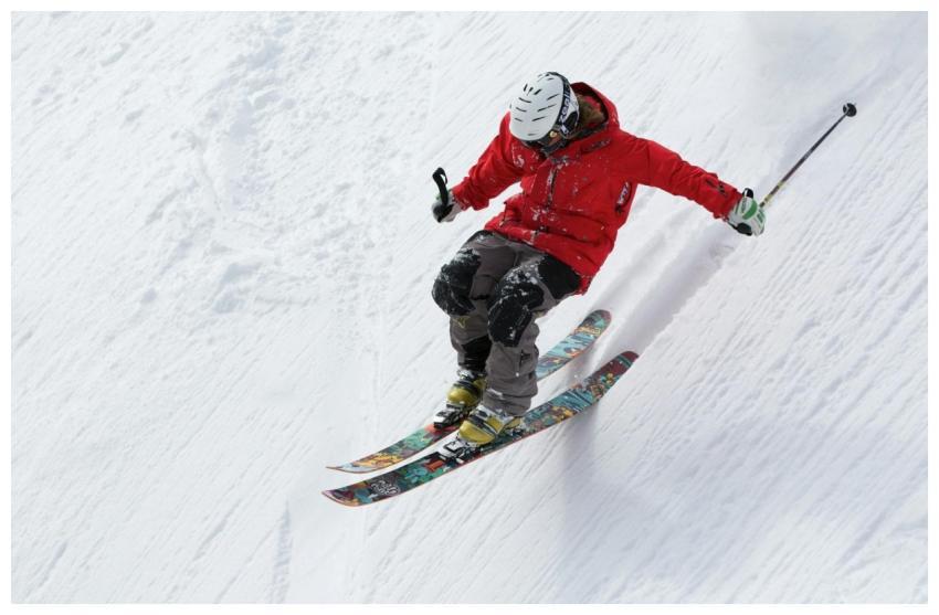A skier in a red jacket descends a steep snowy slo