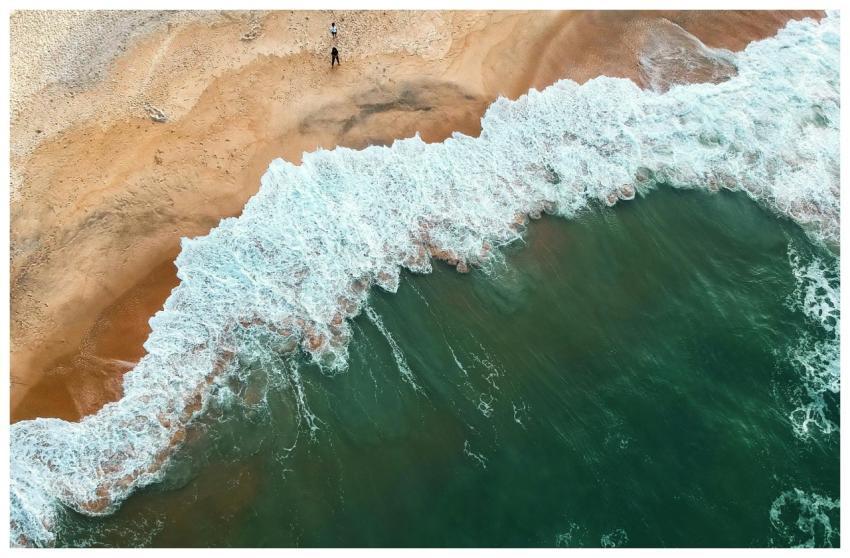Aerial shot of ocean waves crashing onto a sandy b