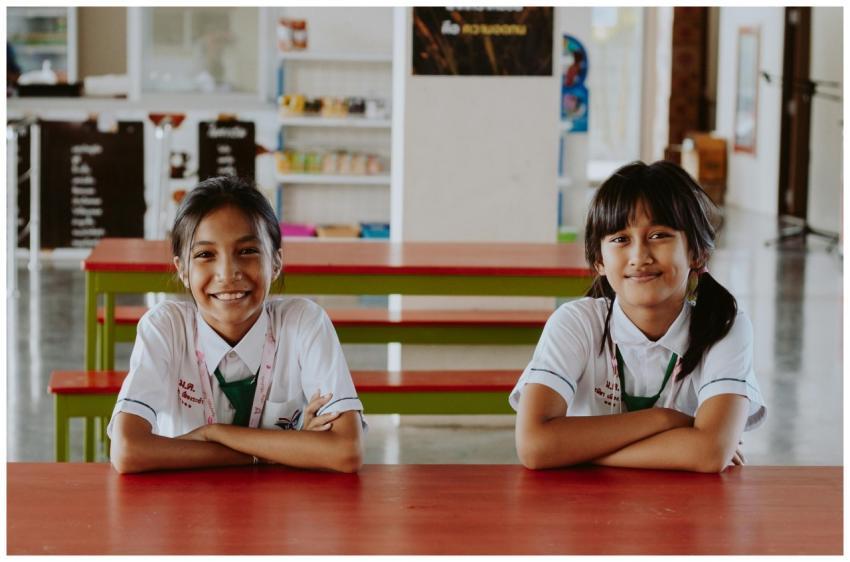 Two school-aged girls smiling while sitting at a t