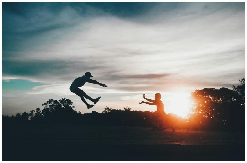 Two silhouetted friends jumping against a vibrant