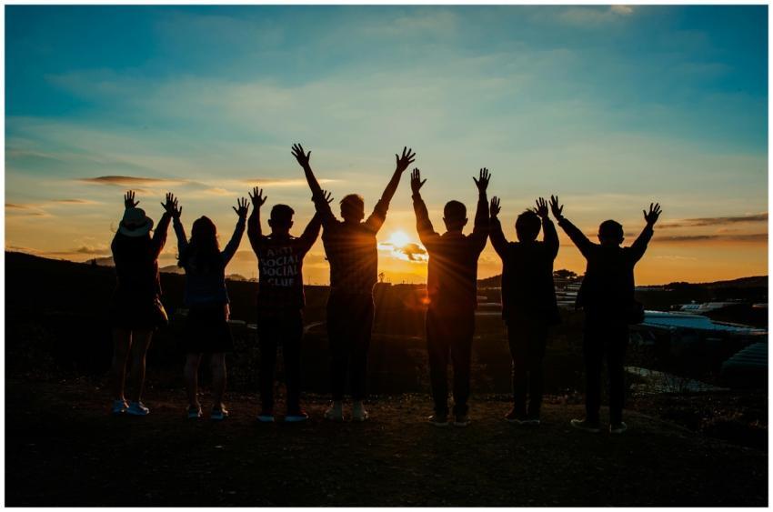 A diverse group of friends raises their arms in ce